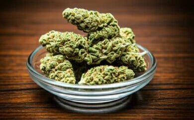Cogollos de cannabis curados y listos para el consumo, presentados en un recipiente de cristal sobre una mesa de madera.